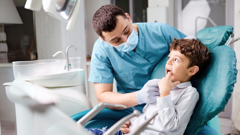 Dentista a observar os dentes de um menino numa cadeira de odontopediatria