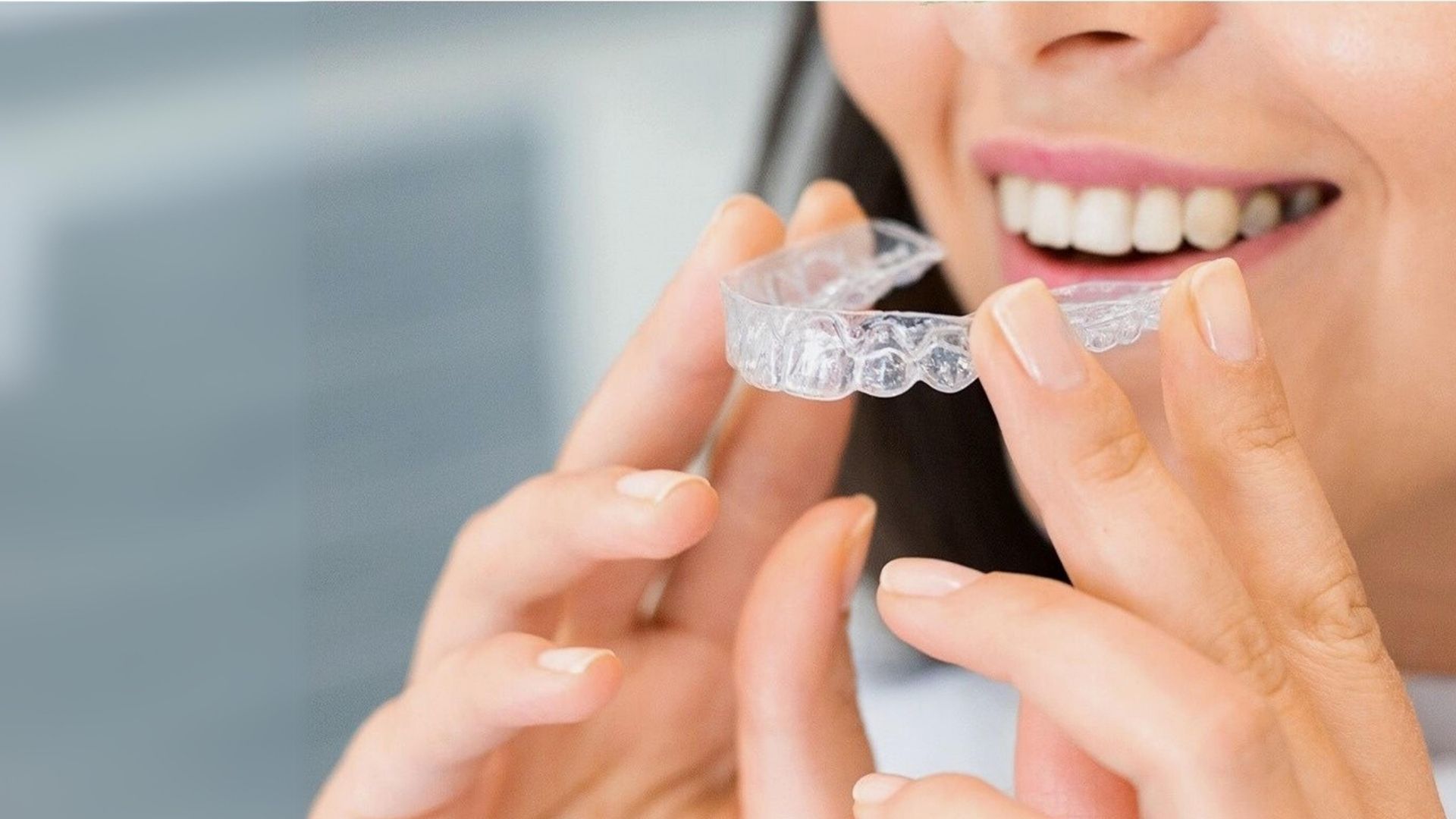 Mulher adulta a segurar um alinhador transparente junto ao sorriso