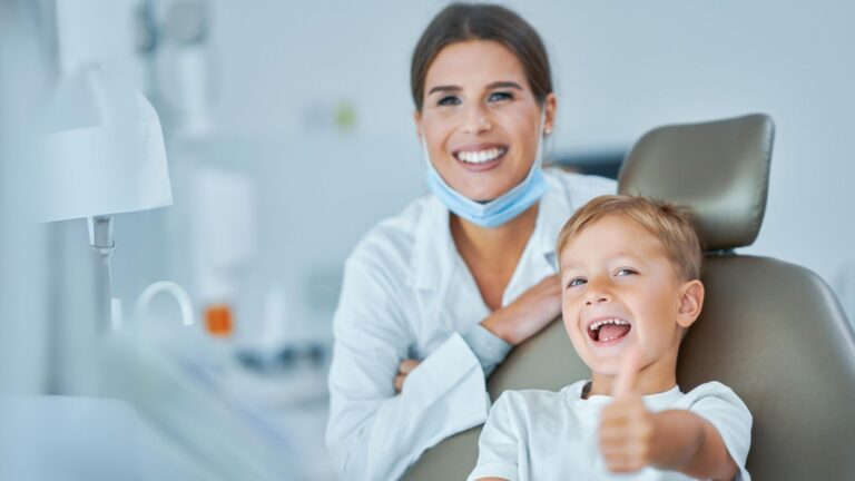 Dentista a sorrir ao lado de uma criança numa consulta dentária
